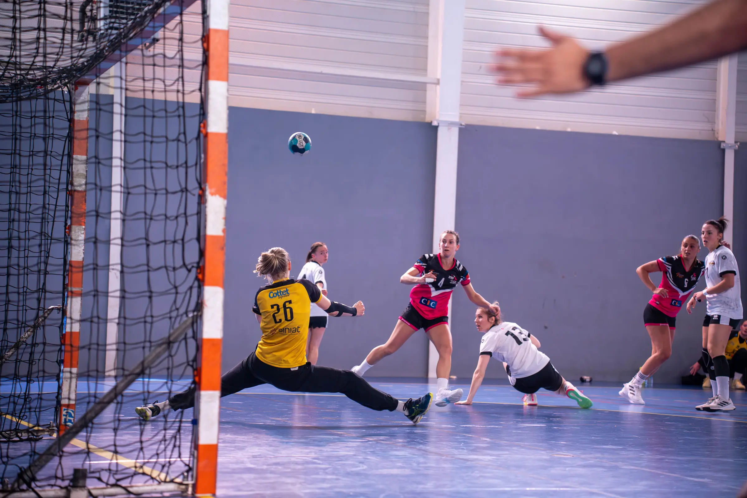 Portera de balonmano estirándose para detener un lanzamiento durante un partido